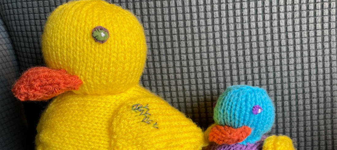 two colourful knitted ducks sitting on a grey sofa