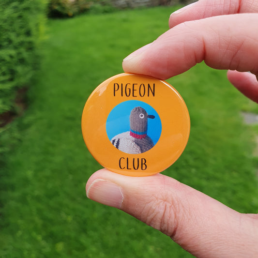 Orange pigeon club knitted pigeon badge being held out in a bright green lawn