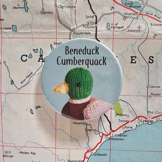 A badge of a knitted mallard duck with the text Beneduck Cumberquack