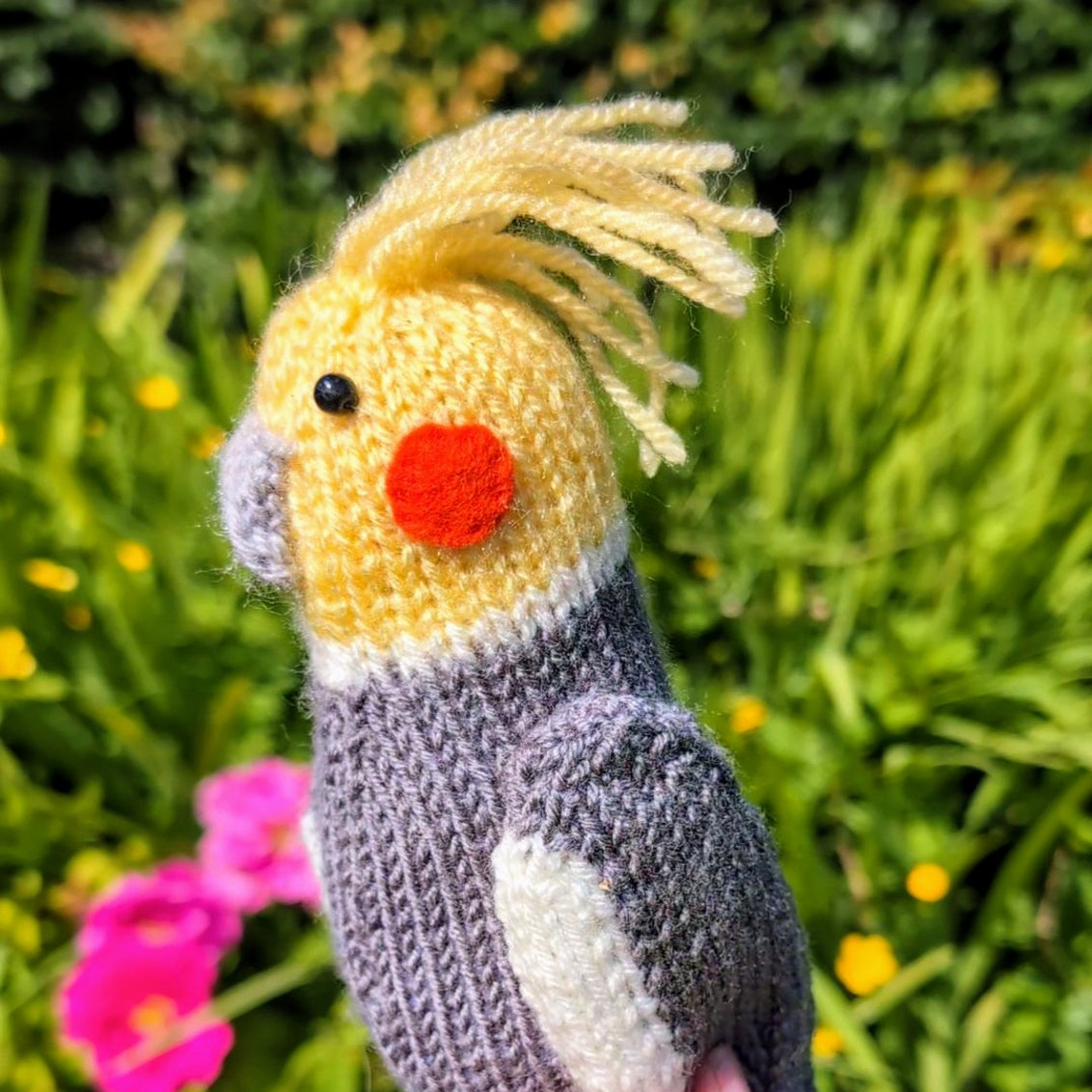 a knitted cockatiel in a colourful garden
