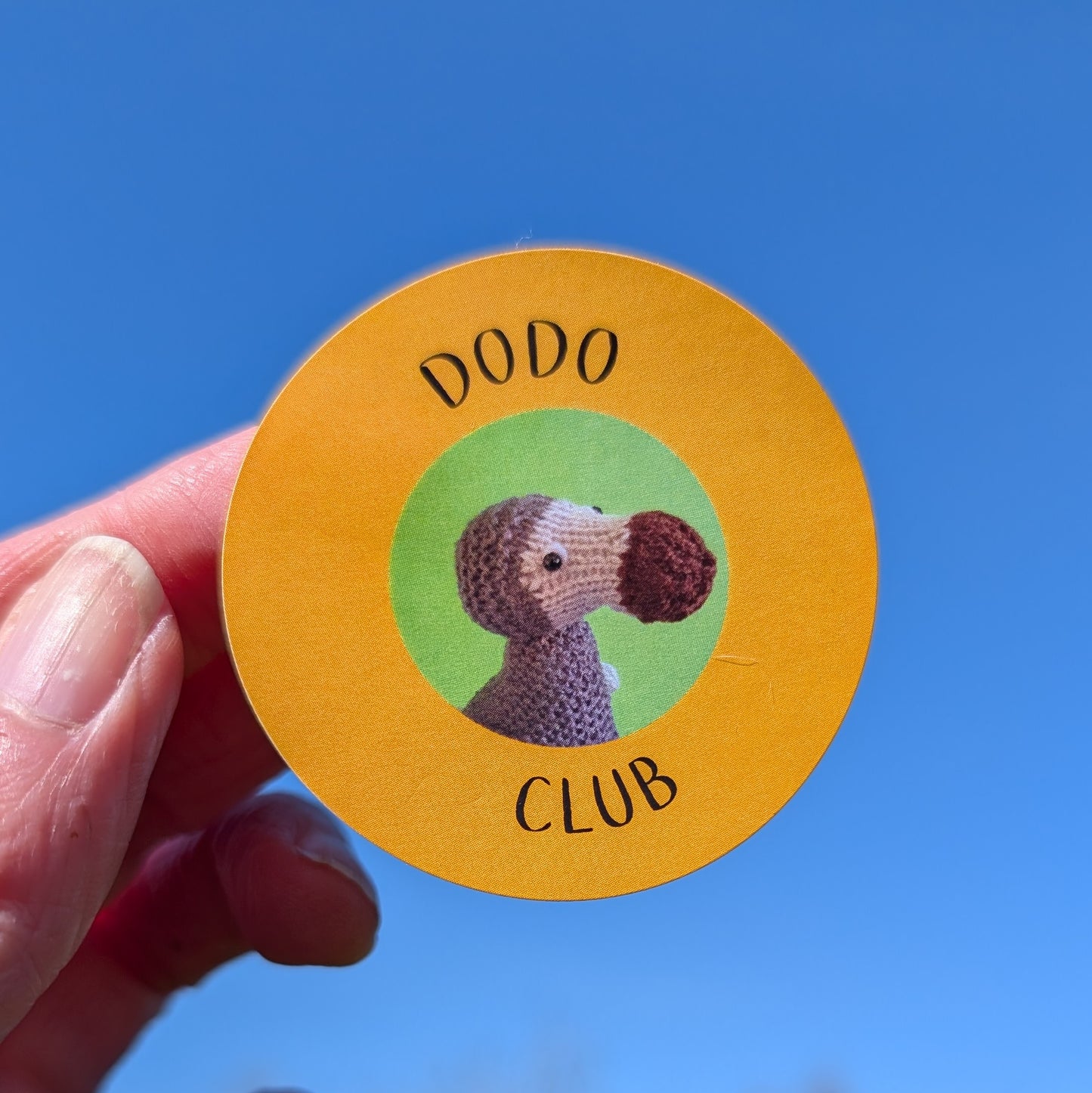An orange sticker with the text Dodo Club and a photo of a knitted dodo on it