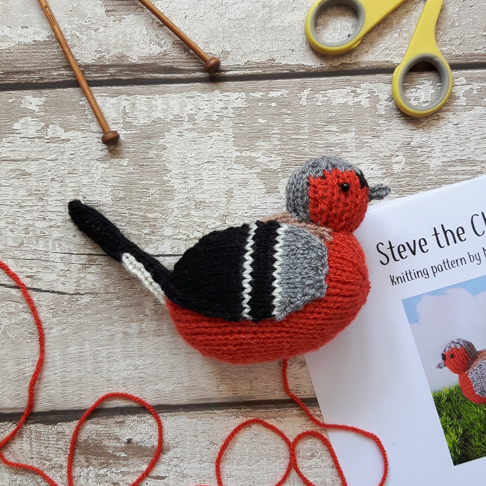 a knitted chaffinch with knitting needles and scissors and a knitting pattern