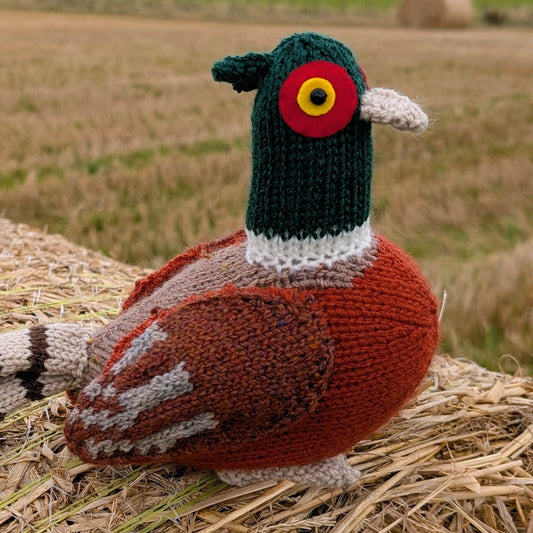 Knitted pheasant sitting on a hay bale with a field in the background